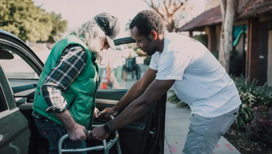 A young man assists a veteran with his walker
