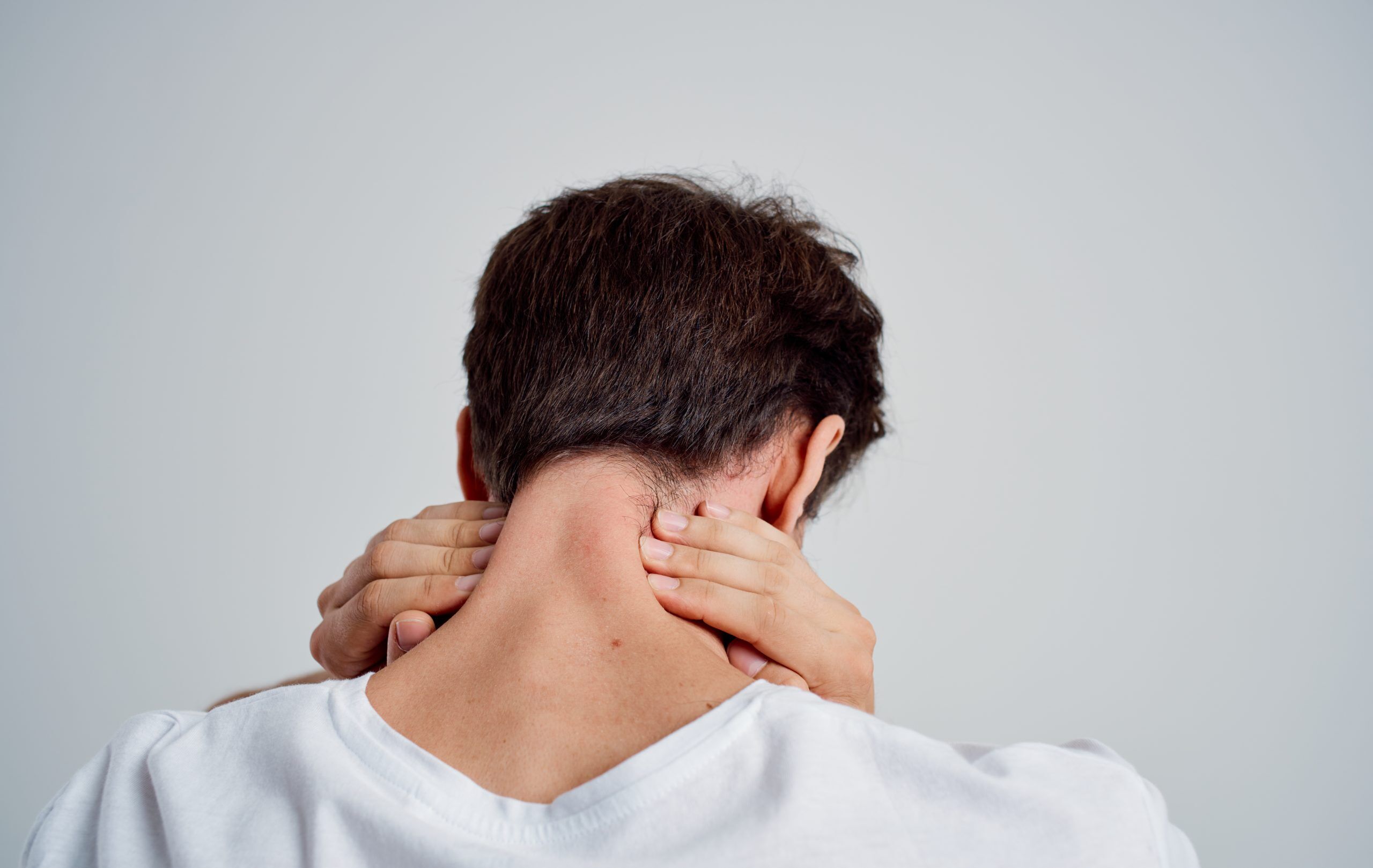 An adult rubbing his neck due to neck pain, prompting the question "Can neck pain cause dizziness​?"
